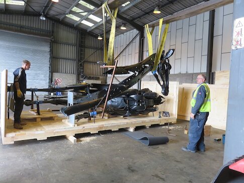 Two workers in a warehouse loading large steel animal parts onto a pallet